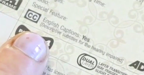 Finger pointing to the text "English Captions: Yes [Descriptive subtitles for the hearing impaired]" on the back of a DVD box