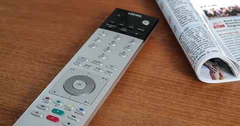 TV remote resting on a flat wooden surface next to an open magazine